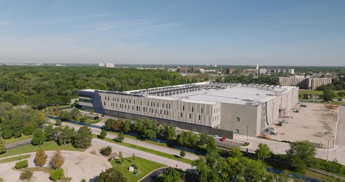Aerial view of a modern data center building surrounded by lush green trees and parking areas in Elk Grove Village, Illinois, United States.