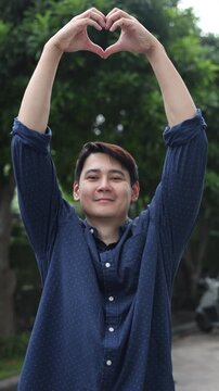 asian man hand make heart shape gesture sign over forest background for save ecology and world concept