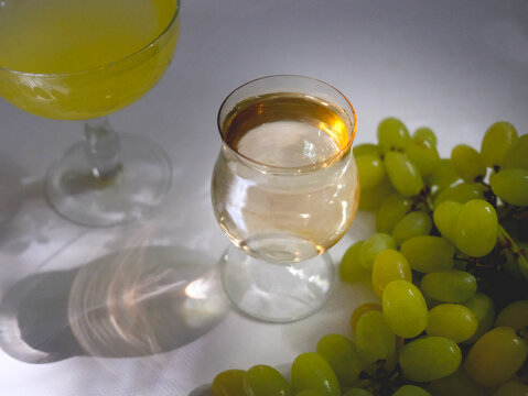 Portuguese green wine Vinho Verde and bunch of green grapes in the wicker basket. Crystal glasswear. Bar counter. Sunlight and shadows on the white table, wall. The warm light of the golden hour.
