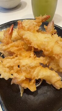 Vertical 4K video moving camera slowly forward toward crispy Japanese deep fried ebi tempura shrimp served on black dish.