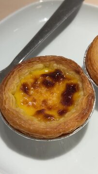 Vertical 4K video moving camera close into golden baked Portuguese egg tart with caramelized custard surface served on plate.