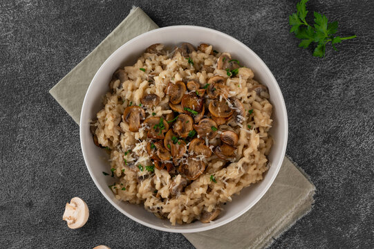 A creamy mushroom risotto topped with parmesan and herbs, served in a white bowl on a dark background. Top view, copy space.
