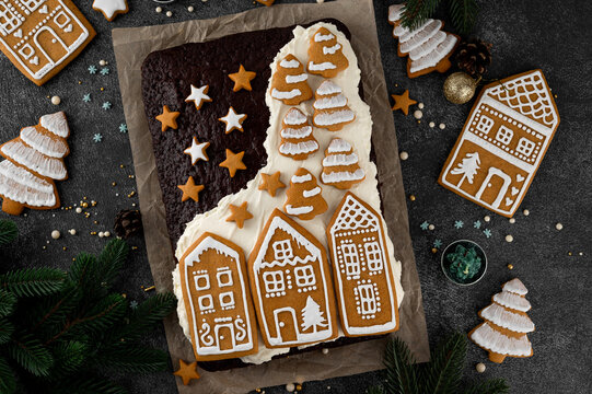Christmas chocolate cake with cream, decorated with gingerbread cookies on top on dark background. Top view, copy space.