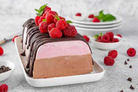 Italian semifreddo ice cream with raspberries and chocolate on a white plate on a concrete background. Summer dessert.