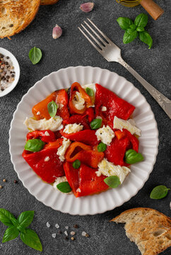 Salad with roasted red peppers and mozzarella in olive oil and garlic on a plate on dark background. Mediterranean appetizer served with bread. Top view.