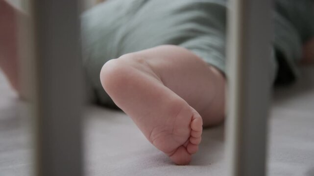 Caucasian infant foot resting inside crib during sleep, filmed in extreme close up. Ideal for newborn healthcare campaigns, pediatric content, and baby product marketing
