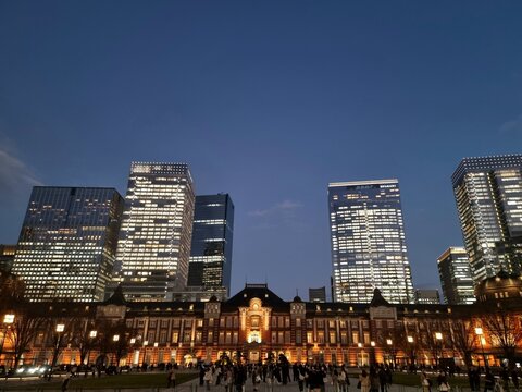 Historic red brick facade of Tokyo Station building with illuminated skyscrapers at night in Marunouchi, Chiyoda, Tokyo, Japan