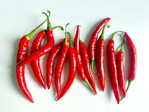 A flat lay arrangement of fresh red Capsicum annuum chili peppers on a clean white background, showcasing vibrant spicy pods and green stems for culinary use.