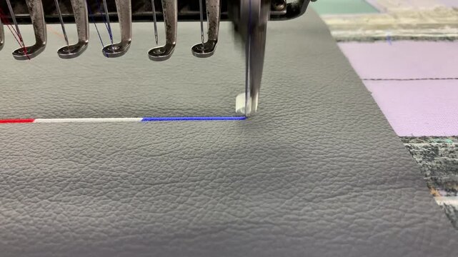 Industrial embroidery machine stitching above on textured synthetic leather material.