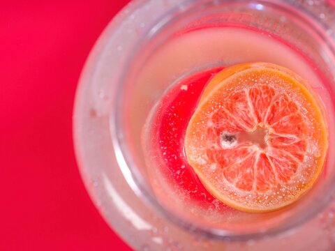 Slice of citrus fruit submerged in clear liquid with visible bubbles and red background