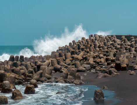 Angler fishing from concrete breakwater blocks as high ocean waves crash against the shore