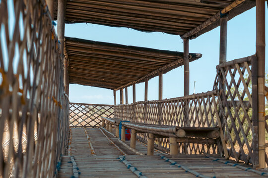 Bamboo bridge walkway with wooden benches and lattice railings under shaded roof