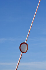 A low angle shot showing a raised red and white striped barrier gate arm with a round road closed sign attached to it against a clear blue sky. © nahhan
