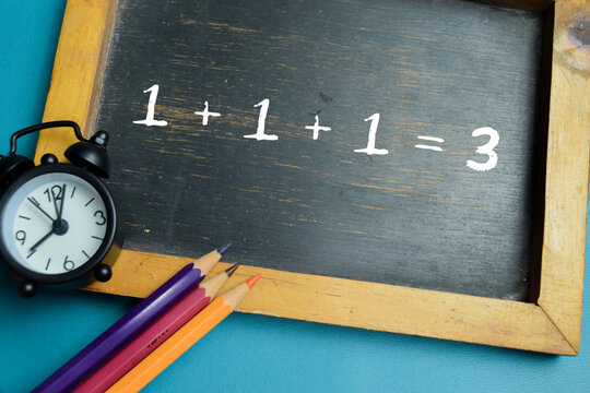 Chalkboard with phrase 1 + 1 + 1 = 3 addition equation on wooden desk. For basic arithmetic and school education