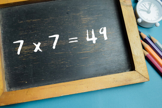 Chalkboard with phrase 7 x 7 = 49 multiplication equation on wooden desk. For basic arithmetic and school education