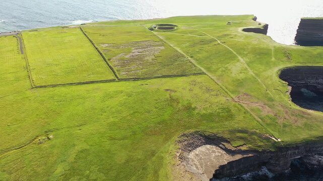 Aerial view of the Dun Briste sea stack featuring dramatic cliffs, green grassy fields, and the Atlantic Ocean in Ballycastle, County Mayo, Ireland.