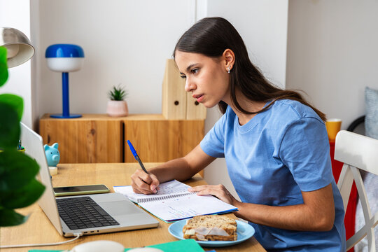 Teenage student girl studying at desk while attending online class at home. Young adolescent doing homework and listening to teacher on laptop video call. Education and e learning concept.