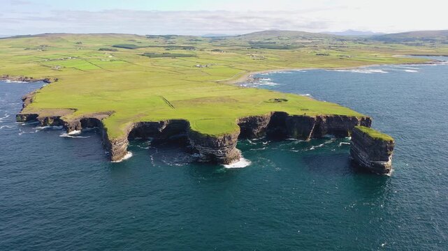 Aerial view of Dun Briste sea stack off the rugged coastline with green grassy cliffs and Atlantic Ocean waves in Ballycastle, County Mayo, Ireland.