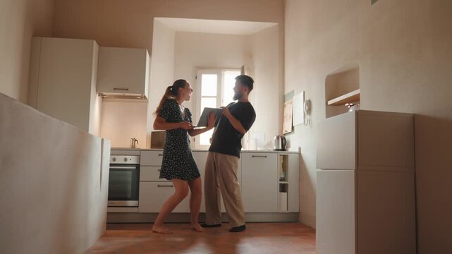 Excited young couple celebrating buying new home, using a laptop and dancing together in the kitchen while planning the renovation and interior design of the apartment