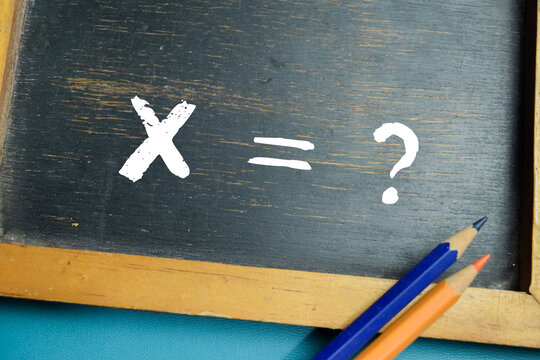 Chalkboard with phrase X equals question mark mathematical equation on wooden desk. For algebra, problem solving, and logic