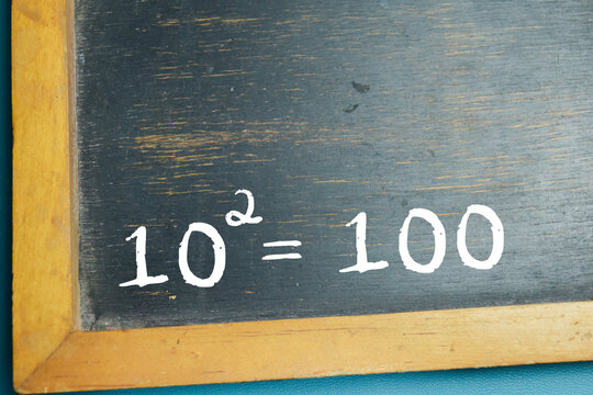 Chalkboard with phrase equation ten squared equals one hundred on wooden desk. For showing powers and arithmetic