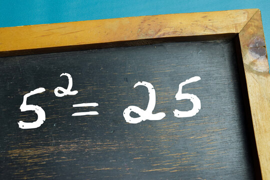 Chalkboard with phrase five squared equals twenty five on wooden desk. For basic algebra