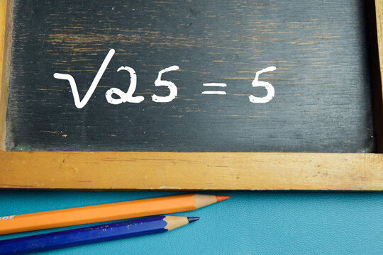 Chalkboard with phrase &radic;25 = 5 square root equation on wooden desk. For basic mathematic arithmetic