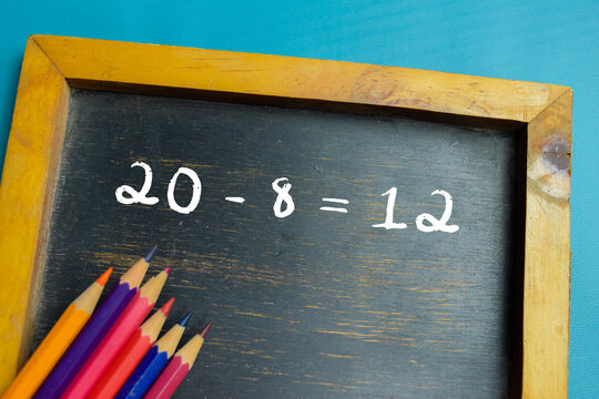 Chalkboard with phrase 20 - 8 = 12 subtraction equation on wooden desk. For basic arithmetic and school education