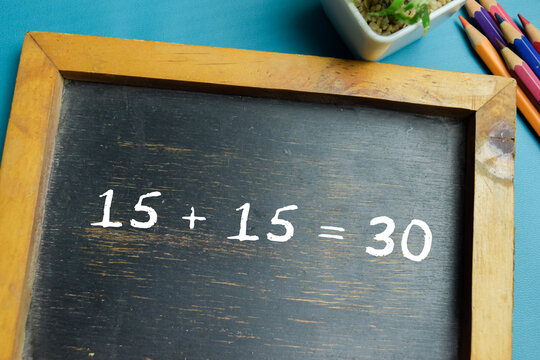 Chalkboard with phrase 15 + 15 = 30 addition equation on wooden desk. For basic arithmetic and school education