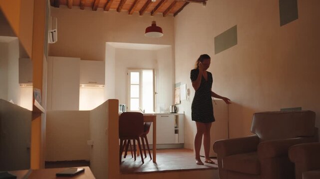 Young stressed woman pacing back and forth in her apartment while having an intense argument on her mobile phone, feeling angry and frustrated during the conversation