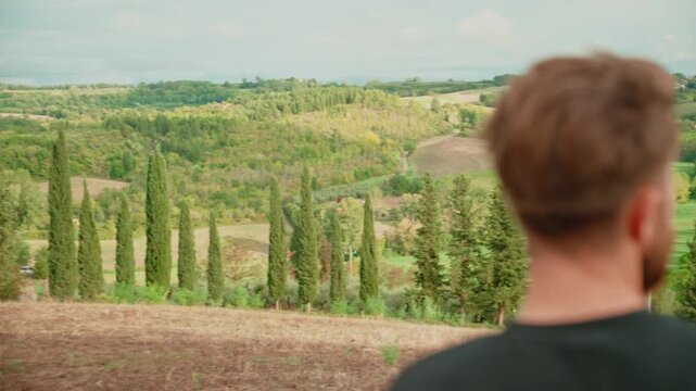 Young bearded man enjoying the stunning view of the rolling green hills and cypress trees of tuscany, italy, feeling a sense of freedom, adventure, and tranquility