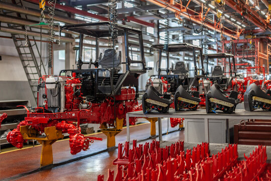 Tractor assembly line in modern heavy machinery manufacturing factory: chassis, cabins, engine components on conveyor-style production line. Heavy industry, large-scale manufacturing, automation.