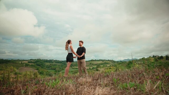 Romantic young couple embracing, kissing, and dancing on a hill surrounded by the picturesque green landscape of tuscany, italy, during a scenic summer holiday vacation