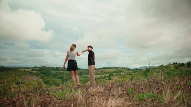 Romantic young couple dancing, laughing, and embracing on a scenic hilltop with beautiful rolling hills of tuscany, italy, enjoying a happy summer vacation together