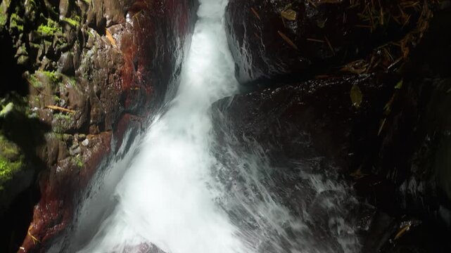 Close up view of clear rushing water cascading over dark wet rocks at Cascade Absalon waterfall in Martinique rainforest