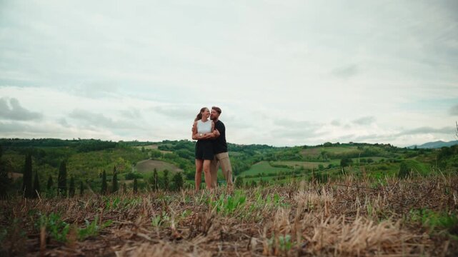 Romantic young couple running toward each other and embracing in a beautiful tuscan landscape, sharing a tender hug and kiss while enjoying their love and togetherness