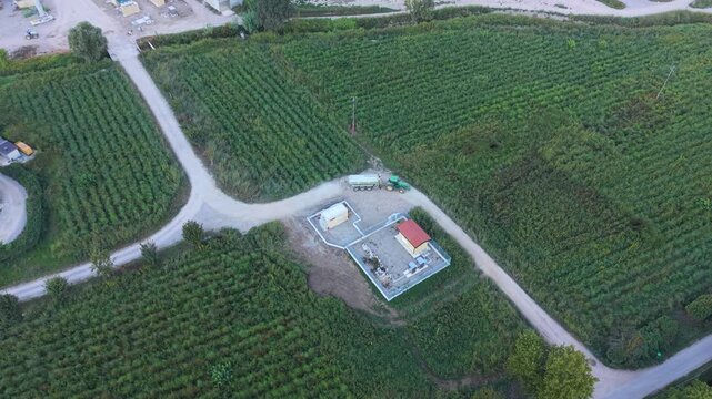 Aerial view of a green tractor pulling a tanker along a dirt road between cultivated fields in Italy, illustrating agricultural transport, fertilizer application and sustainable farming practices.