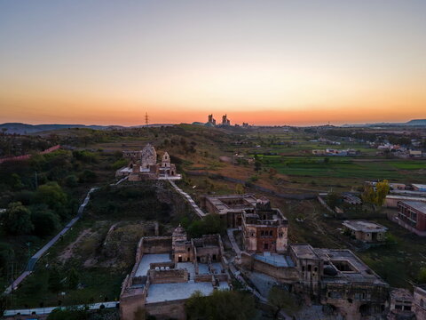 Aerial view of Katas Raj Temple Complex featuring ancient stone structures and courtyards surrounded by rural landscape and fields under a soft sunset sky in Katas, Punjab, Pakistan.