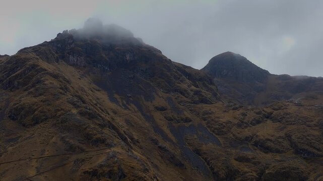Cinematic aerial view of rugged Andean mountain peaks shrouded in low-hanging clouds and dense mist, showcasing the dramatic, moody landscape in Cusco, Peru.