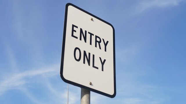 Slow motion landscape of an Entry Only regulatory sign mounted on a metal pole meaning vehicles can use it to enter but are not permitted to exit one-way traffic flow in public carpark infrastructure