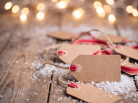 Rustic kraft paper gift tags tied with string resting on a wooden surface dusted with artificial snow.