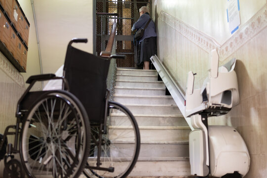 Elderly woman with disability and a wheelchair using the assistance of a stair lift like a mobility help technology