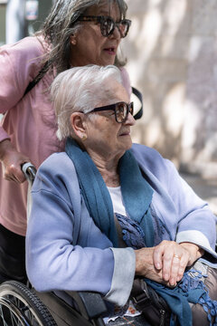 Daughter carefully pushing her senior mother in a wheelchair, providing essential support and companionship outdoors, illustrating the bond of family and dedicated elder care