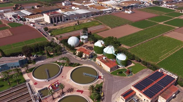 Wastewater treatment plant with biogas digesters, circular settling tanks, solar panels, and surrounding agricultural fields viewed from above