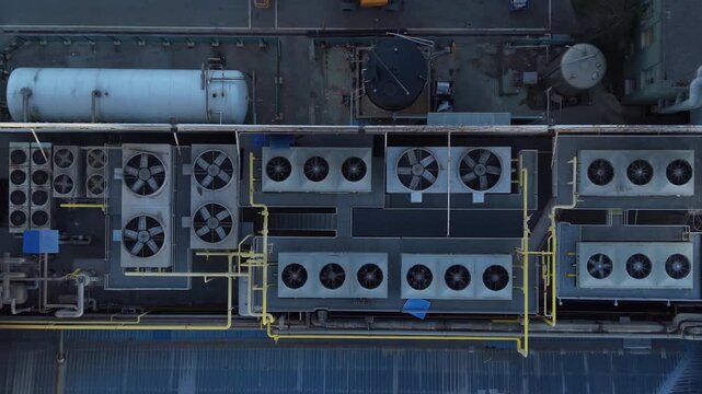 Top-down view of industrial rooftop HVAC units with large cooling fans, yellow pipework and pressure tanks on a factory or commercial building