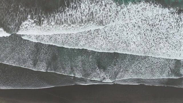 Aerial view of powerful ocean waves crashing onto a dark volcanic black sand beach in Costa Rica.