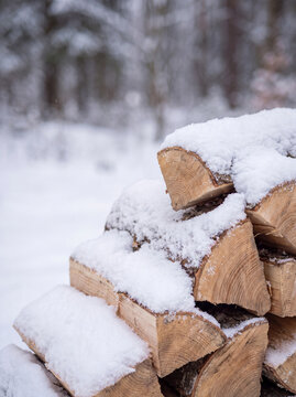 Neat pile of chopped hardwood logs and firewood covered with a thick blanket of fresh white snow outside in winter