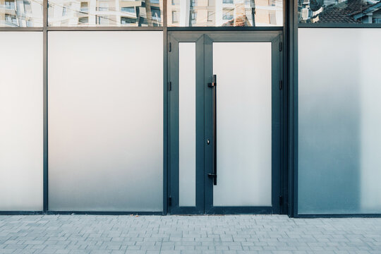 Modern building entrance featuring a dark framed glass door and surrounding frosted windows, reflecting urban architecture