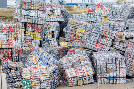 Compressed aluminum cans form dense metal bales stacked at recycling facility. Industrial waste processing scene shows scrap recovery, sorting, reuse, sustainability, circular economy and resources