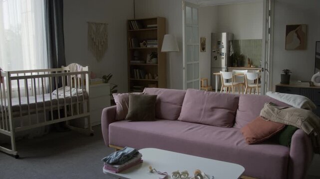 Modern apartment interior showcasing infant crib, couch, and baby accessories. Footage serves parenting campaigns, family lifestyle advertisements, and real estate nursery promotions